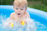 Cute little child bathing with duck in blue street pool in courtyard